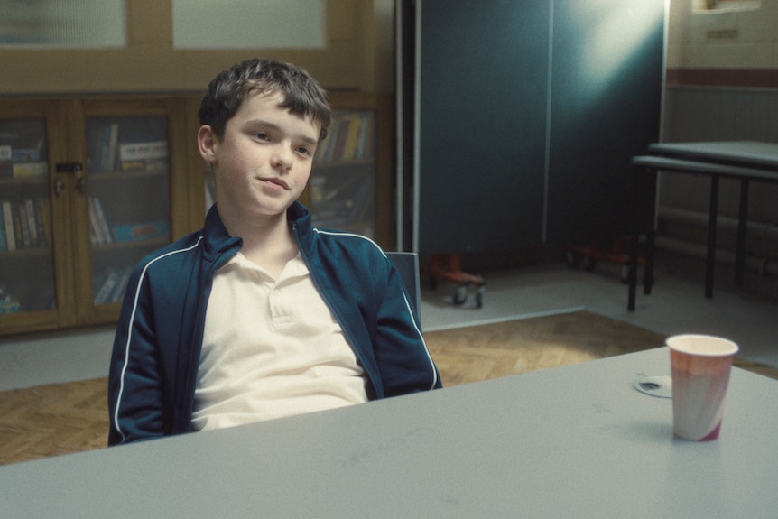 Owen Cooper leans back in a chair and smirks while acting in Adolescence.