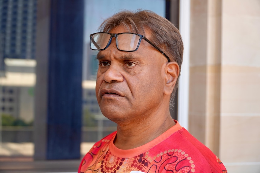 A man with a pair of glass on his forehead wears a red colour top