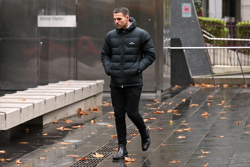 A man dressed in a black puffer jacket and bluck pants walks outside court.