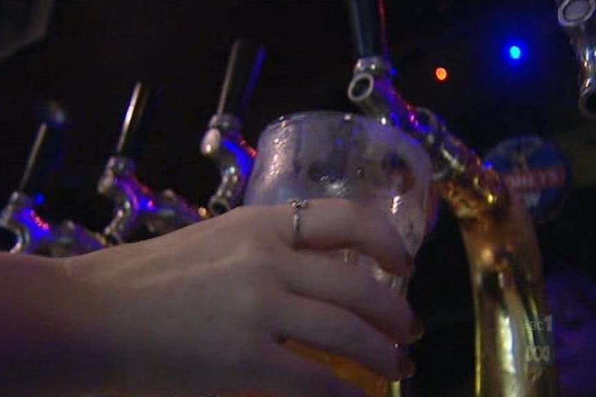 A hand holding a glass up to a beer tap.