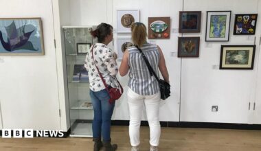Two women stand in front of a selection of artworks mounted on the white walls of Goole Museum gallery