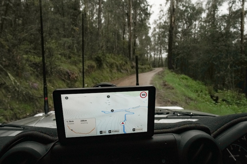 A view through a windscreen shows a GPS map on the dashboard, aerials on the bonnet, as car drives down dirt track