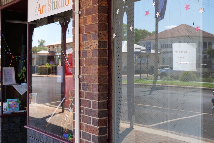 An empty shopfront with a sign in the window saying shop for rent next to an art studio. 