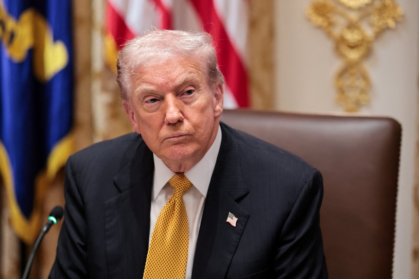 A man in a suit looks on while sitting in a chair.