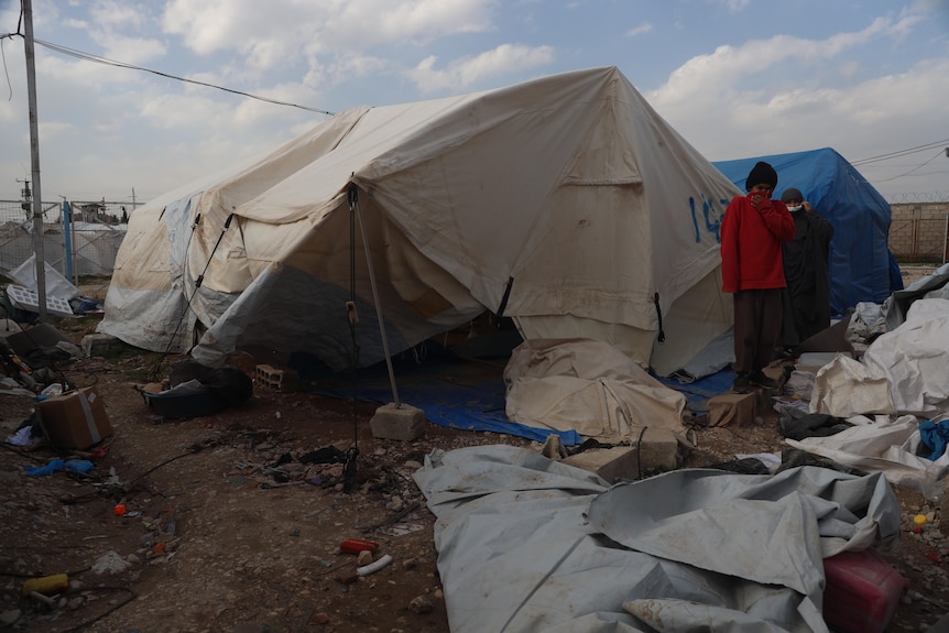 A tent in the rubble with a child in a red shirt