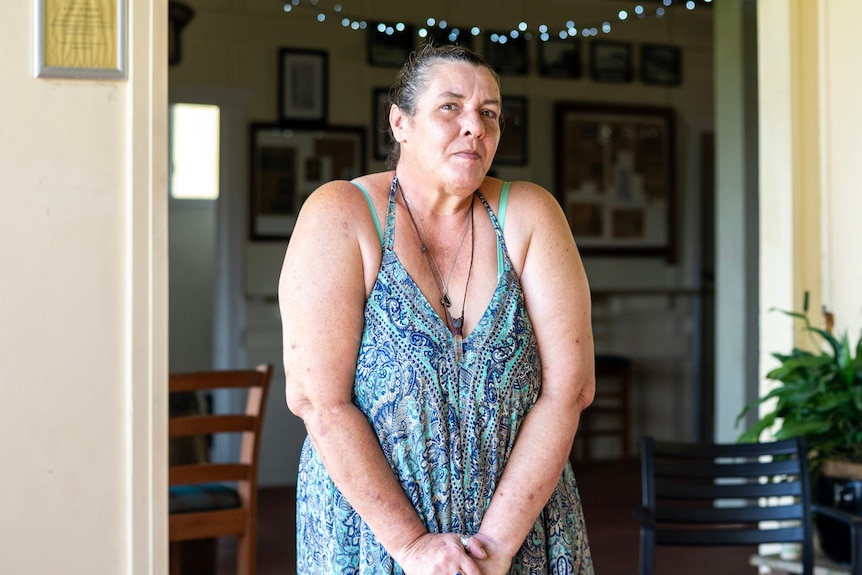 A woman leans on a walking cane on a verandah.