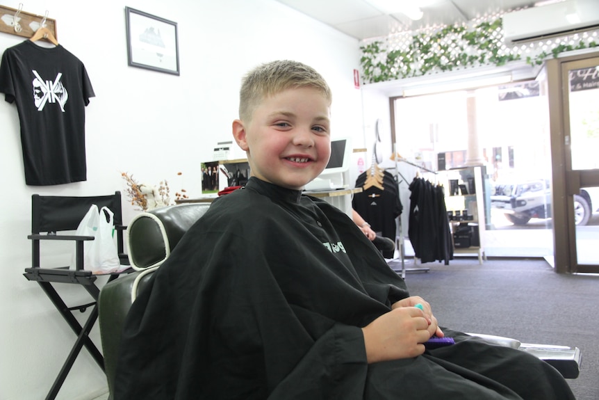 A boy sitting in a hairdresser's chair.
