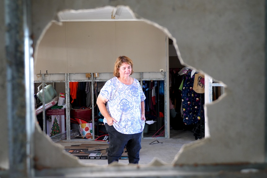 Melinda Byrne standing in her empty house pictured through a hole in the wall.
