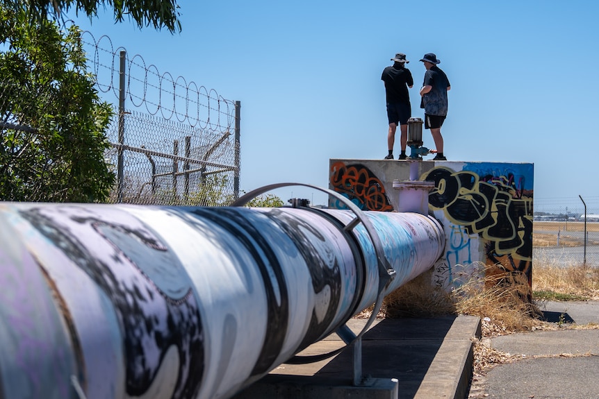 Two men standing on a concrete block with a large pipe coming from it