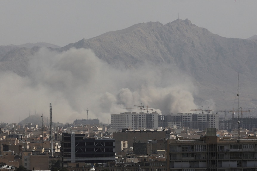 smoke rising from between buildings with a mountain backdrop