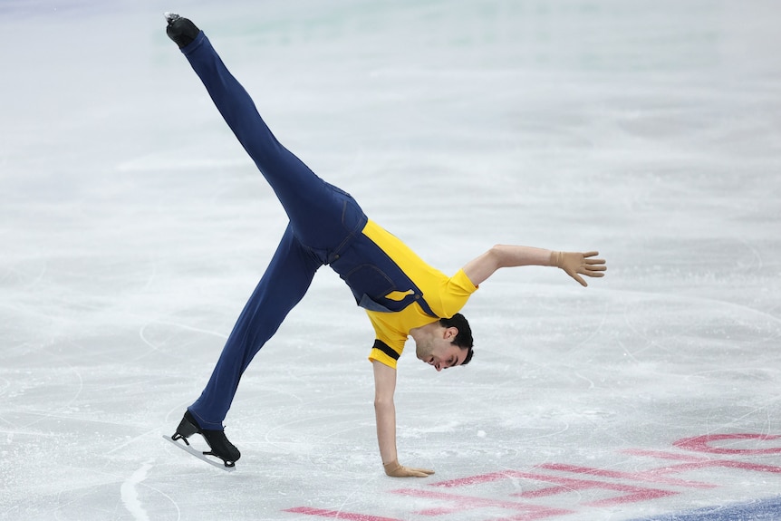 Male figure skater performing on the ice, right hand on the ice, one leg in the air