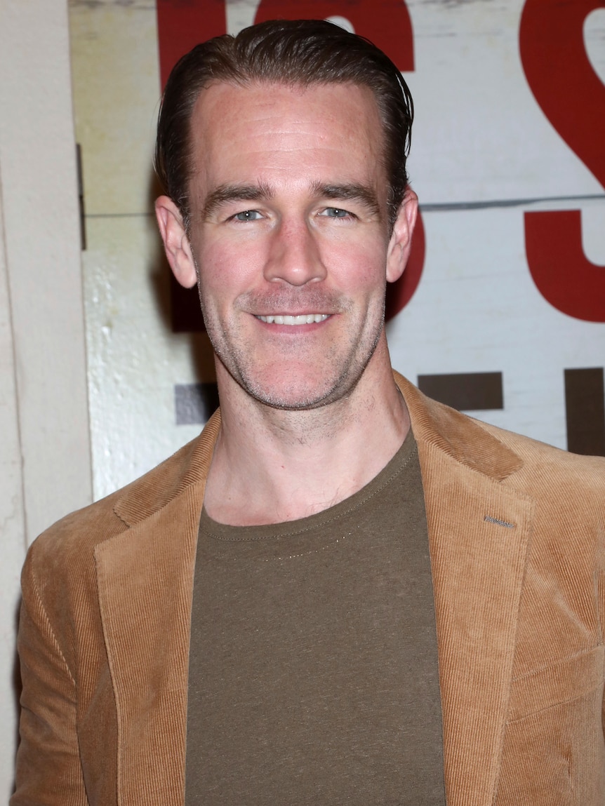 Actor James Van Der Beek dressed in brown suit jacket and casual khaki colored sweater.