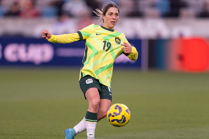 A Matildas player looks across field as she plays the ball during an international match.