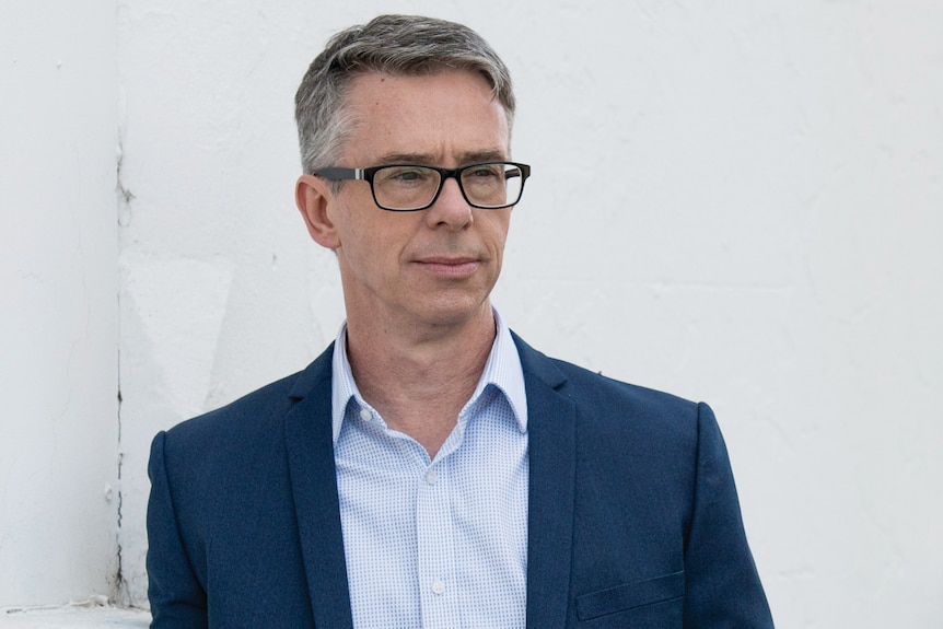 man in a blue suit with greying hair and glasses 