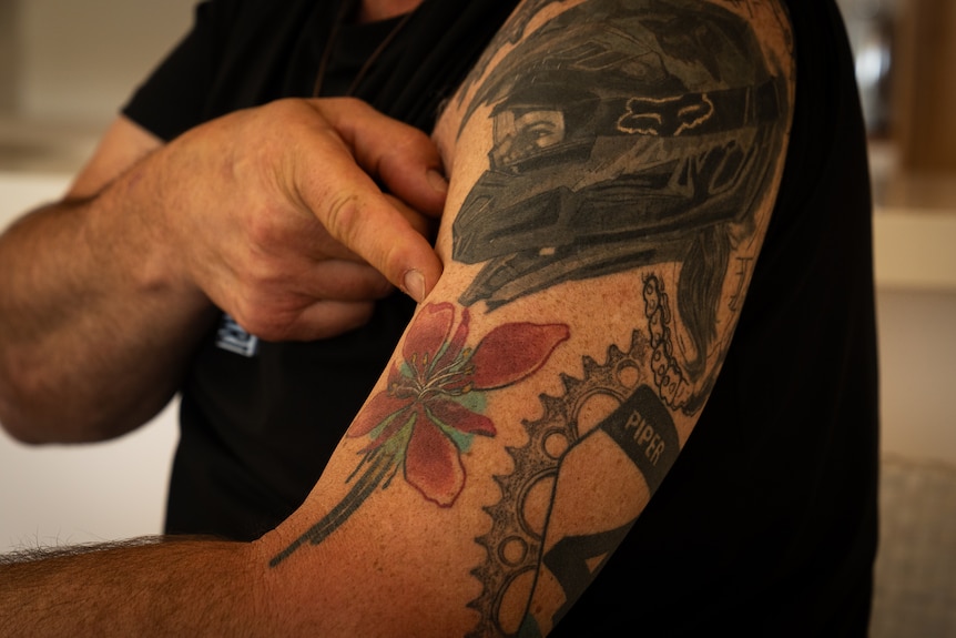 Mans bicept with tattoos, a young womans face in a dirt bike helmet, a flower, a sprocket, chain ring and race number