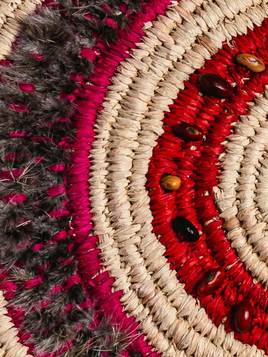 A close-up shot of an artwork woven in circles. The colours are red, black and beige.