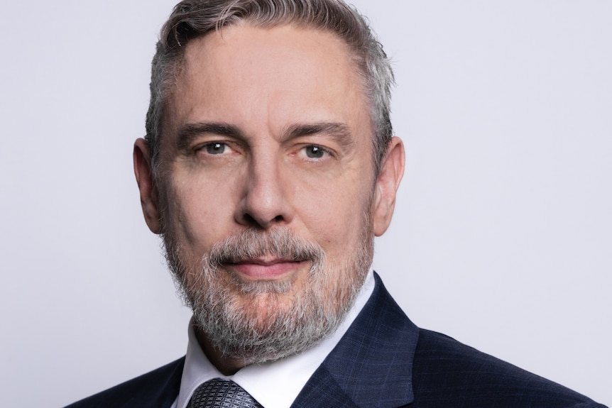 A portrait shot of David Young, a man with grey hair and a beard in a suit.