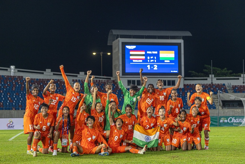 Members of the Indian women's football team pose for a photo where they raise arms triumphantly and celebrate