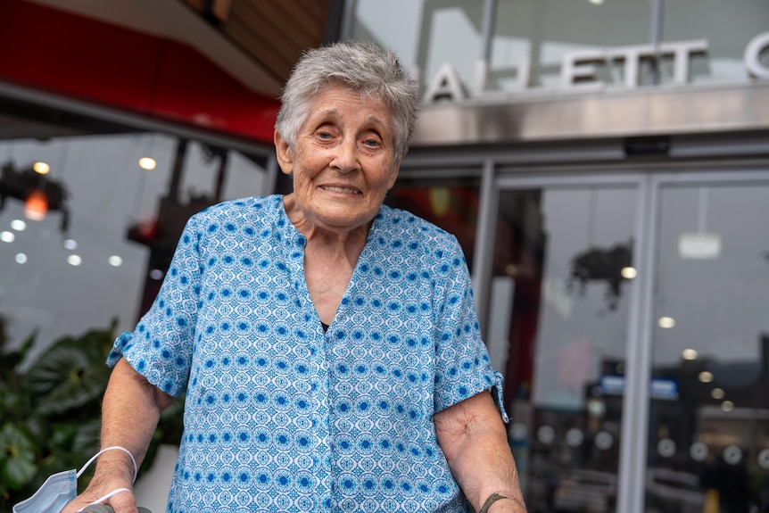 An elderly woman with a walker outside the glass doors of Hallett Cove shopping centre