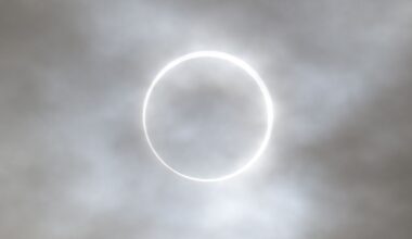 The edge of the sun is visible around the silhouette of the moon during an eclipse, forming a burning ring behind a veil of thin clouds.