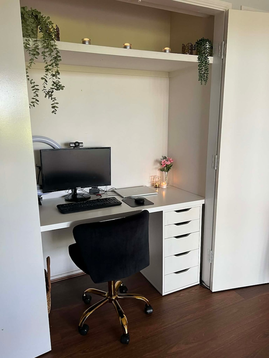 A white computer desk and chair inside a cupboard, decorated with candles and greenery