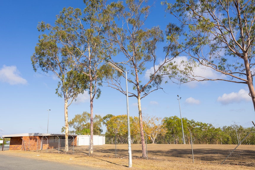 A fenced field with trees and a small brick building
