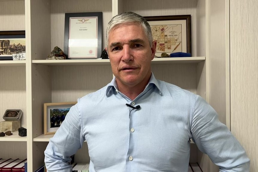 Robbie Katter, hands on his hips, stands before a bookshelf.
