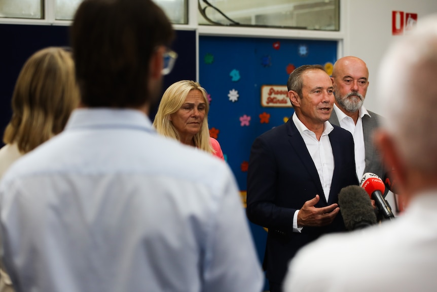 WA Premier Roger Cook speaking into microphones at a media conference, surrounded by other people.