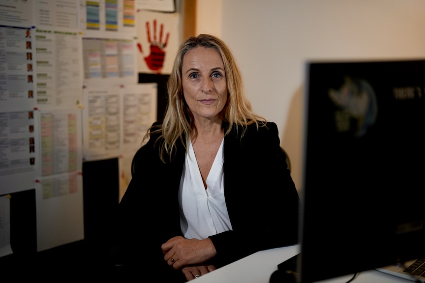 Sue Higginson in a black suit with a white top at her desk in an office.