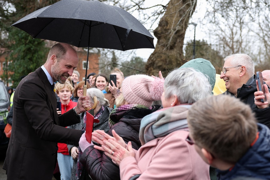 Prince William holds an umbella while he greets members of the public who have gathered to see him.