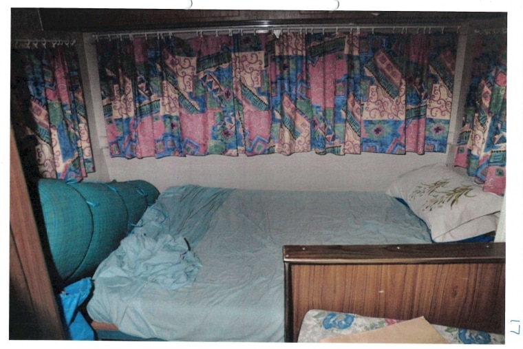 The interior of a caravan, shows a bed with walls around it and patterned curtains.