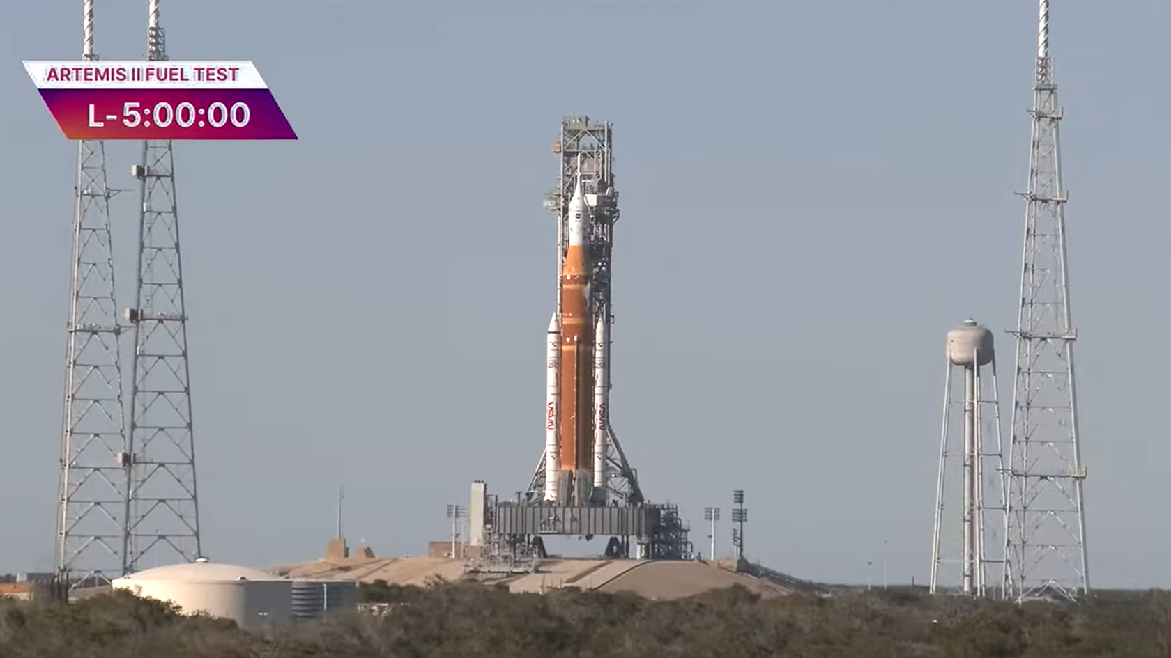 an orange rocket stands against a pale sky.