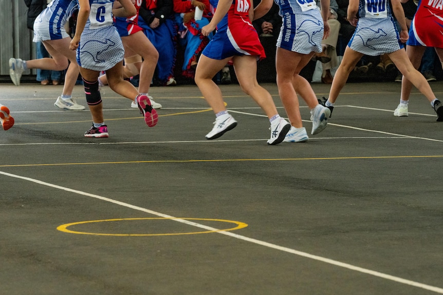 Netballers running around on a court, seen from the waist down.