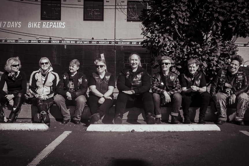 Motorbike riders sitting on bench.