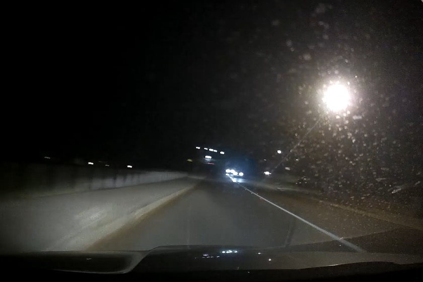 Dashcam footage at night showing a road with headlights in the distance. 