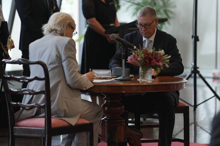 Two officials sitting at a table, signing official documents.