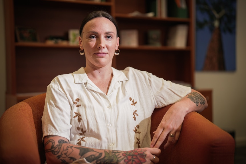 A woman sitting in a chair, wearing a serious facial expression.