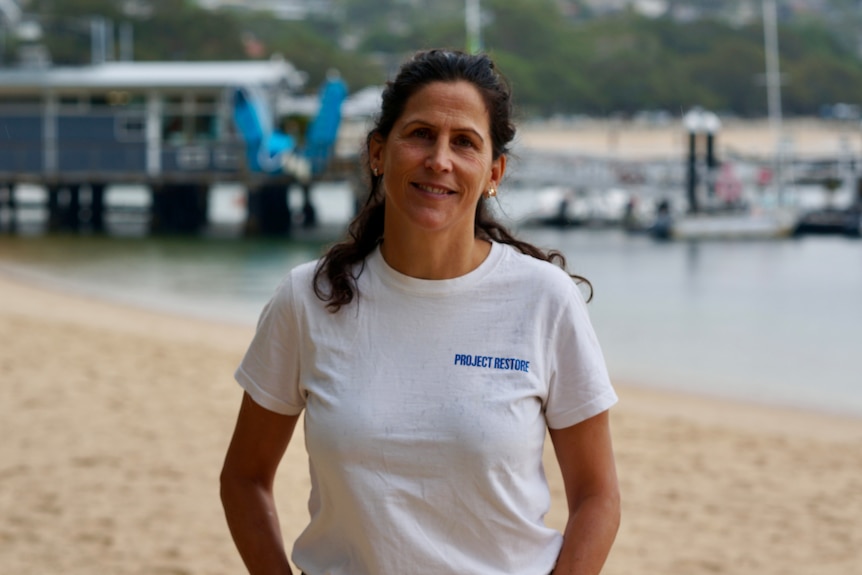 Adriana Burgers has dark hair and a light shirt, and stands in front of a harbour jetty.