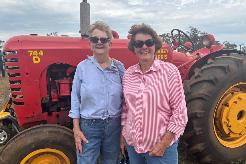Two women stand in front of a large old tractor. 