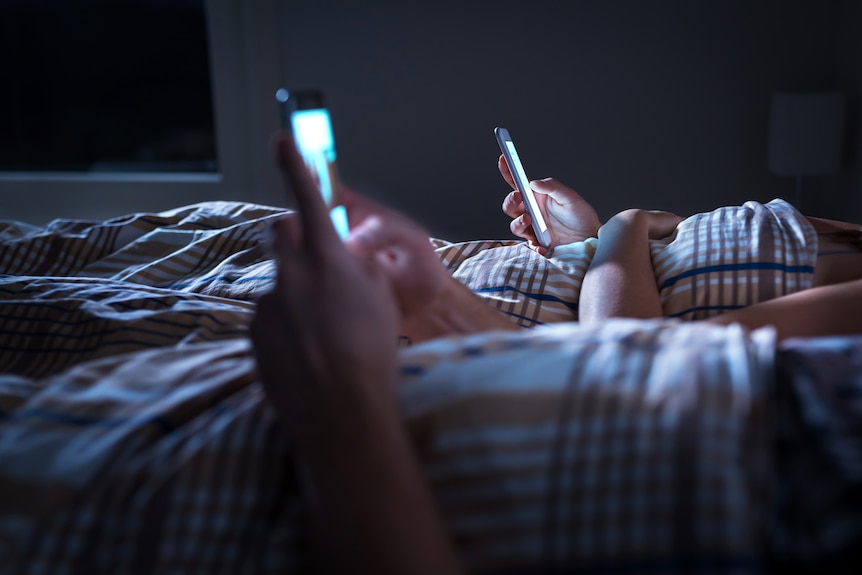 Two people on their phones in bed.