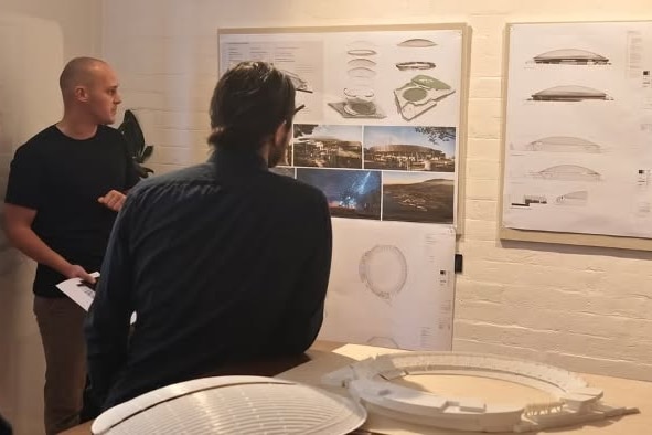 Two people in an office looking at plans and designs of a stadium project.