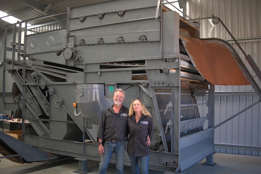 man and woman standing smiling at camera in front of big square machine