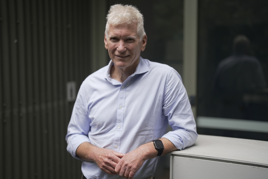 Older man in a light blue shirt and chinos standing outside.