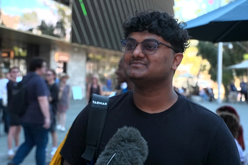 A man with a dark shirt glasses pauses in the street for an interview