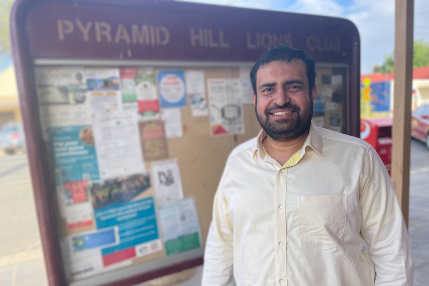 A tanned man with a beard wearing a light yellow shirt standing in front of a Pyramid Hill Lions Club sign