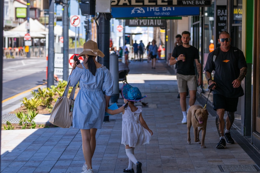 A woman and a girl walk on a paved footpath