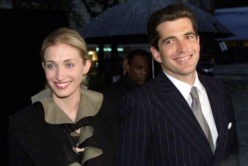 A smiling blonde woman andf a dark-haired man outdoors on a rainy night.