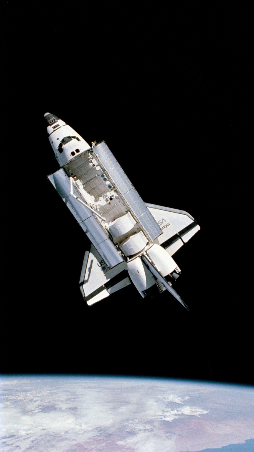 Photo taken in space of a space shuttle, its large doors open, with the curved Earth at the bottom of frame.