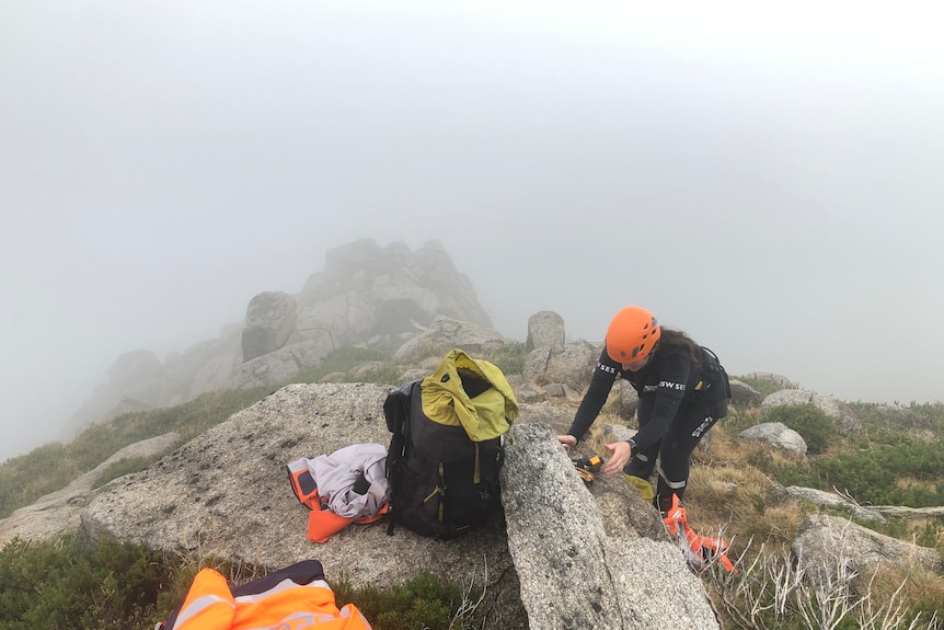 A rescue operator in a helmet, in a foggy rocky landscape.