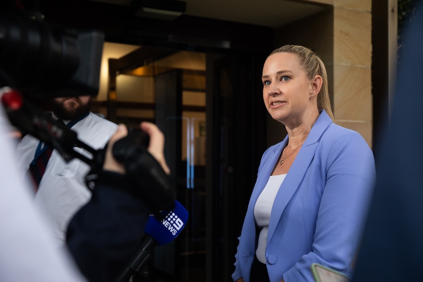Michelle Maynard stands in front of a doorway speaking to reporters.